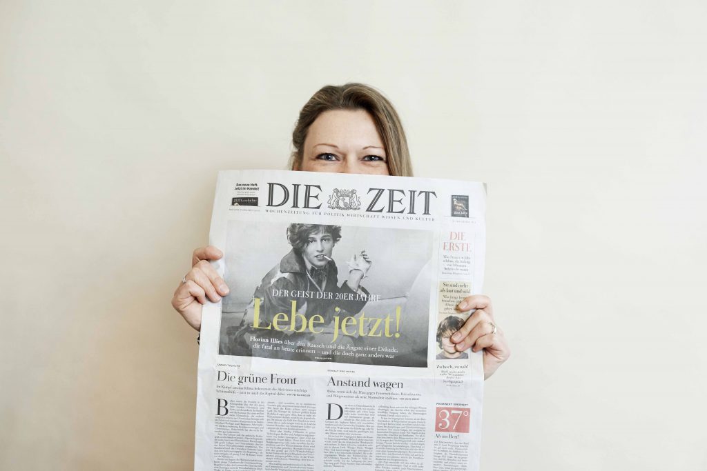 Eine Person hebt eine Zeitung vor ihr Gesicht