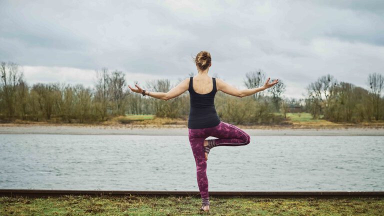 Eine Person steht in einer Yogapose am Rhein