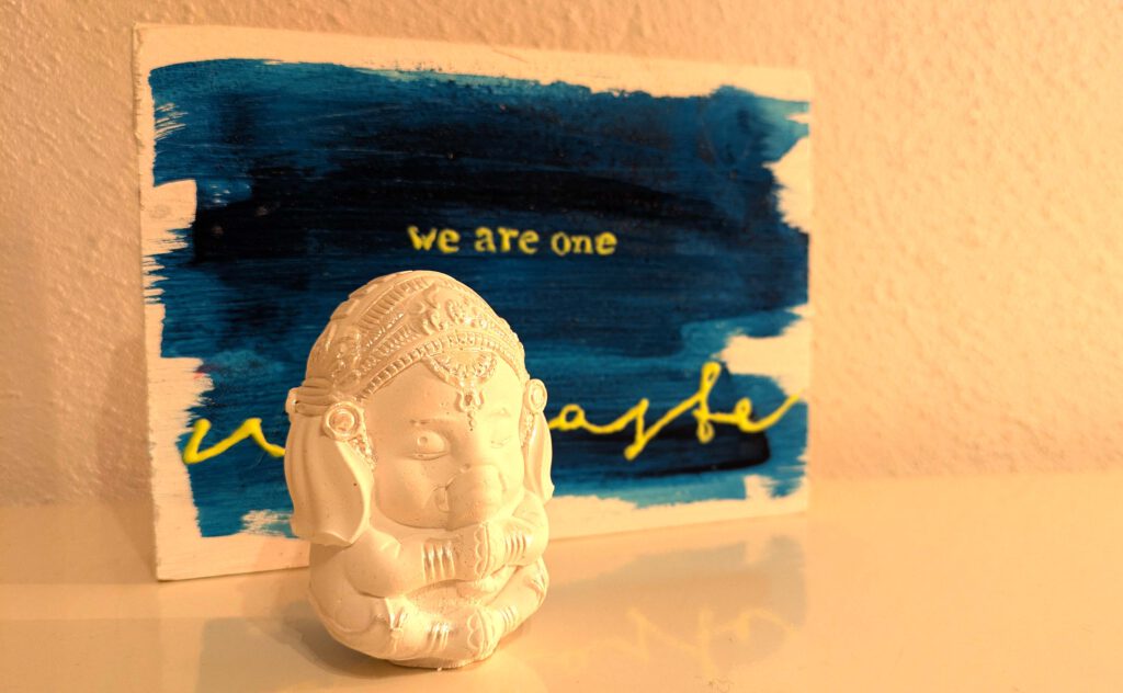 Eine Ganeshafigur vor einem Schild mit der Aufschrift "We are one - Namaste"